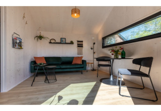 Gezellige leefruimte in Tinyhouse «La Mouette» in Nederland met groene zetel, eettafel en raam.
