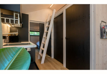 Intérieur du Tinyhouse «La Mouette» aux Pays-Bas avec kitchenette, échelle de mezzanine et portes noires.