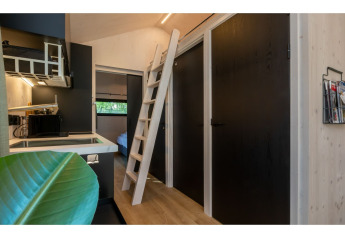 Intérieur du Tinyhouse «La Mouette» aux Pays-Bas avec kitchenette, échelle de mezzanine et portes noires.