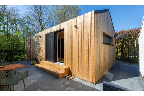Moderne tiny house ‘La Mouette’ in Nederland met houten bekleding, terras en groene omgeving.