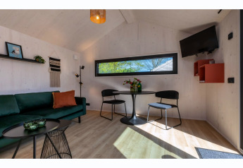 Intérieur lumineux du Tinyhouse «La Mouette» aux Pays-Bas avec canapé vert et coin repas moderne.