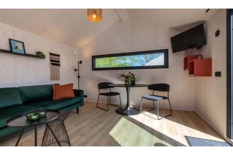 Licht interieur van Tinyhouse «La Mouette» in Nederland met groene zetel en eettafel.