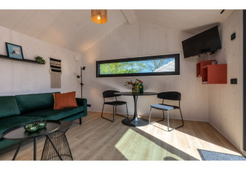 Intérieur lumineux du Tinyhouse «La Mouette» aux Pays-Bas avec canapé vert et coin repas moderne.