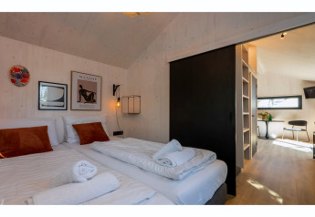 Chambre moderne dans Tinyhouse La Mouette aux Pays-Bas avec deux lits, des œuvres murales et vue sur le séjour.