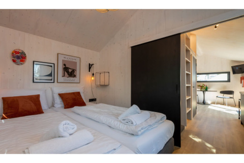 Moderne slaapkamer in Tinyhouse La Mouette met twee bedden, kunst aan de muur en uitzicht op leefruimte.