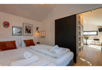 Chambre moderne dans Tinyhouse La Mouette aux Pays-Bas avec deux lits, des œuvres murales et vue sur le séjour.
