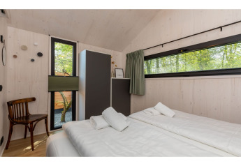 Chambre lumineuse du Tinyhouse «La Mouette» aux Pays-Bas avec lit double, armoire et vue sur la forêt.