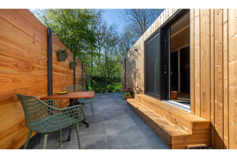Buitenterras aan Tinyhouse La Mouette in Nederland met houten wanden, tafel, stoelen en groene omgeving.