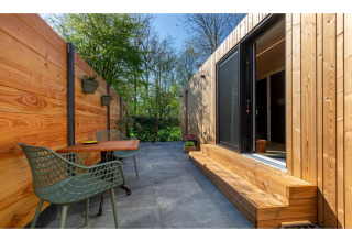 Buitenterras aan Tinyhouse La Mouette in Nederland met houten wanden, tafel, stoelen en groene omgeving.