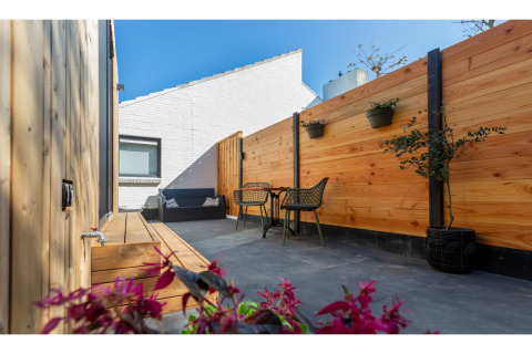 Knus terras bij Tinyhouse La Mouette in Nederland met houten omheining, zitjes en bloempotten.