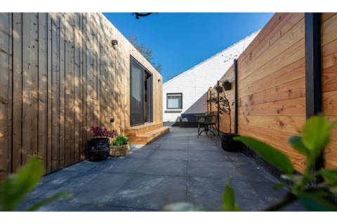 Buitenterras met houten wandbekleding en tegels bij Tinyhouse «La Mouette» in Nederland met blauwe lucht.