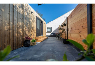 Buitenterras met houten wandbekleding en tegels bij Tinyhouse «La Mouette» in Nederland met blauwe lucht.