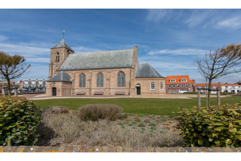 Uitzicht op een historische kerk en moderne huizen vanuit de tuin van Tinyhouse «La Mouette» in Nederland.