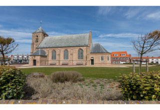 Uitzicht op een historische kerk en moderne huizen vanuit de tuin van Tinyhouse «La Mouette» in Nederland.