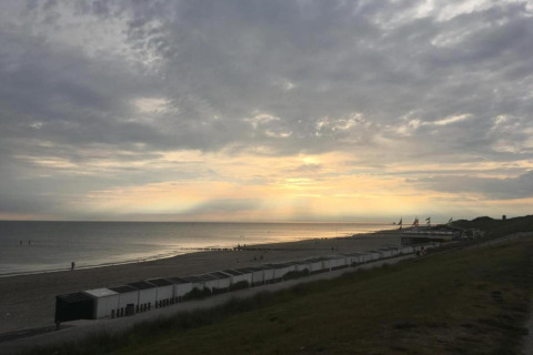 Strandzonsondergang vanuit Tinyhouse «La Mouette» in Nederland, met kleine huisjes en wolkenhemel.