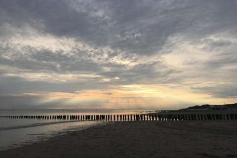 Strand bij zonsondergang, bewolking en paalhoofden gezien vanuit Tinyhouse «La Mouette» in Nederland.