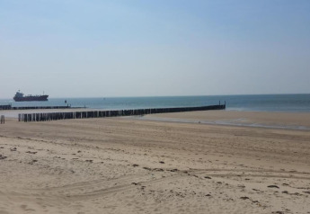 Plage de sable paisible avec des poteaux en bois et un bateau au loin, vue depuis Tinyhouse La Mouette.