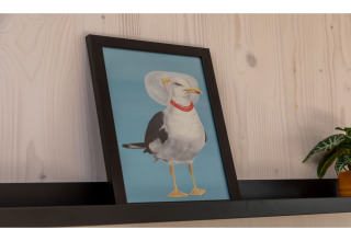 Ingelijste foto van een meeuw met een dierenkraag en rode halsband, staand op een zwarte plank in een tiny house.