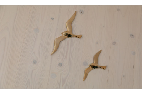 Twee gouden vliegende vogeldecoraties op een lichte houten wand in Tinyhouse «La Mouette», Nederland.