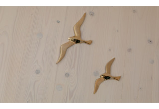 Twee gouden vliegende vogeldecoraties op een lichte houten wand in Tinyhouse «La Mouette», Nederland.