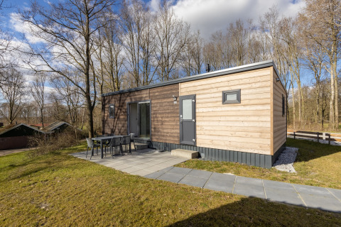 Moderne lodge i træ ved Hunzepark 13 med terrasse og udendørs spisebord omgivet af natur og skov.