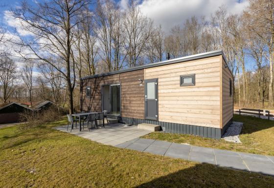 Moderne lodge i træ ved Hunzepark 13 med terrasse og udendørs spisebord omgivet af natur og skov.