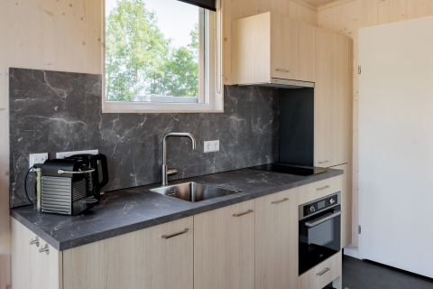 Modern, compact kitchen with a black marble countertop and wooden cabinets in a tiny house in the Netherlands.