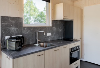 Modern, compact kitchen with a black marble countertop and wooden cabinets in a tiny house in the Netherlands.