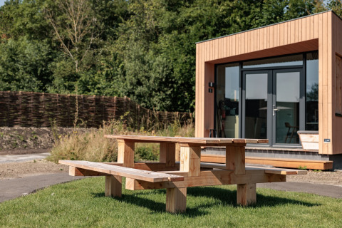 Wooden picnic table on grass in front of a modern tiny house at Résidence De Banjaard 22, Netherlands.