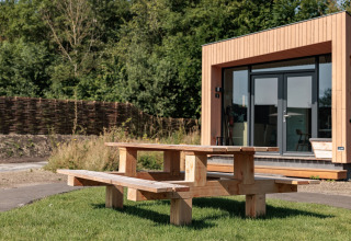 Wooden picnic table on grass in front of a modern tiny house at Résidence De Banjaard 22, Netherlands.