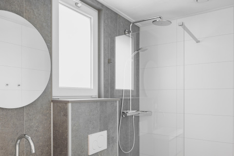 Modern bathroom with rain shower, round mirror and bright window inside a tiny house in the Netherlands.