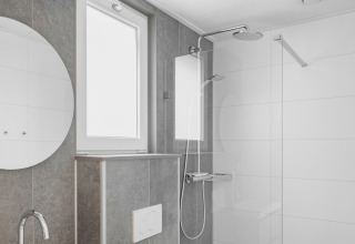 Modern bathroom with rain shower, round mirror and bright window inside a tiny house in the Netherlands.