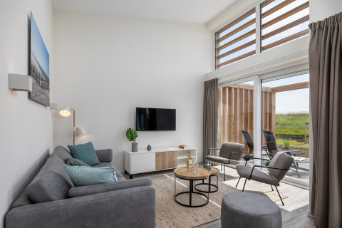 Lichte, moderne woonkamer in lodge Water Village 4 in Nederland met grote ramen en uitzicht op de tuin.