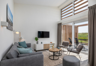 Lichte, moderne woonkamer in lodge Water Village 4 in Nederland met grote ramen en uitzicht op de tuin.