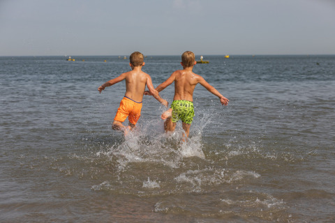 Two children run into the sea at the beach near the tiny house 'Noordzee' Résidence De Banjaard 22 in the Netherlands.