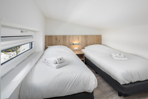 Lichte, moderne slaapkamer met twee eenpersoonsbedden in de Water Village 4 lodge in Nederland.