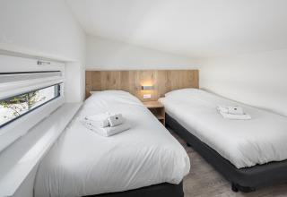Lichte, moderne slaapkamer met twee eenpersoonsbedden in de Water Village 4 lodge in Nederland.