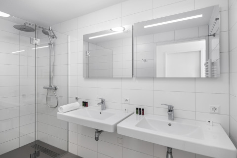 Moderne badkamer bij Water Village 4, Nederland, met dubbele wastafels, spiegels, douche en witte tegels.