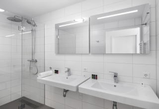 Moderne badkamer bij Water Village 4, Nederland, met dubbele wastafels, spiegels, douche en witte tegels.