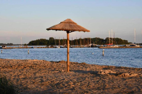 Sandy beach with straw sunshade by the water, boats and pier in background at Noordzee, Netherlands.