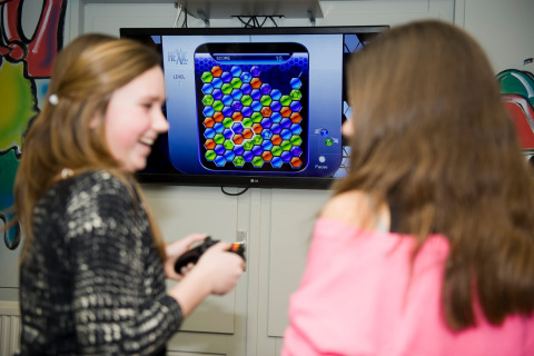 Twee meisjes lachen terwijl ze samen een kleurrijk puzzelspel spelen op televisie in een lodge.