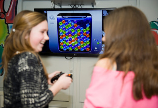 Twee meisjes lachen terwijl ze samen een kleurrijk puzzelspel spelen op televisie in een lodge.