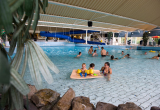 Overdekt zwembad bij een lodge met volwassenen en kinderen die spelen, en een blauwe glijbaan op de achtergrond.