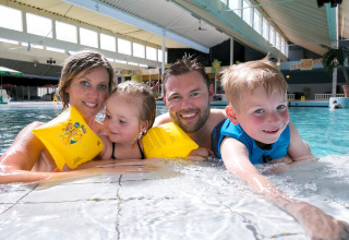 Blije familie samen in het binnenzwembad van een lodge, kinderen dragen zwembandjes en zwemvest.