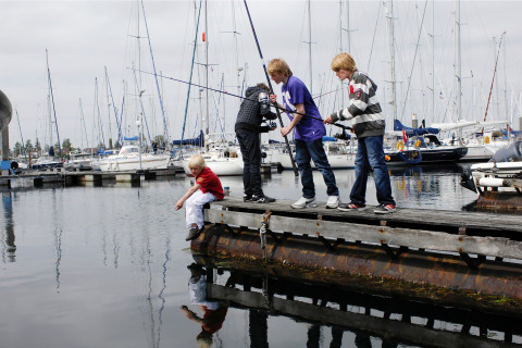 Vier kinderen vissen op een steiger bij Water Village 4 in Nederland, omringd door zeilboten in de haven.