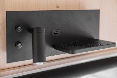 Modern black wall panel with USB port, adjustable reading light, shelf, and two round switches in a tiny house.