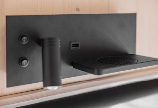 Modern black wall panel with USB port, adjustable reading light, shelf, and two round switches in a tiny house.