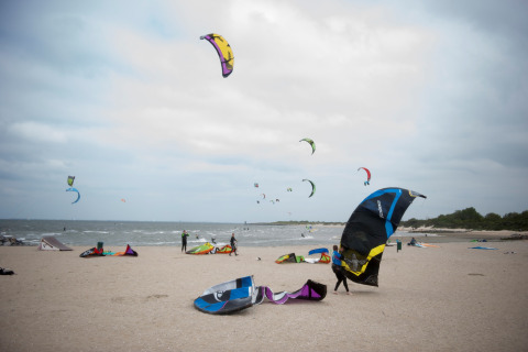 Mensen zijn aan het kitesurfen en maken hun kites gereed op een strand bij een lodge onder bewolkte lucht.
