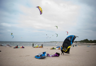 Mensen zijn aan het kitesurfen en maken hun kites gereed op een strand bij een lodge onder bewolkte lucht.