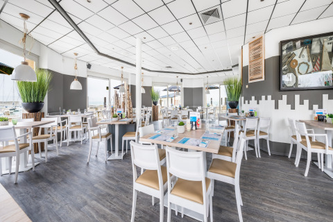 Lichte, moderne lodge-restaurant met witte stoelen, houten vloer, grote ramen en groene kamerplanten.